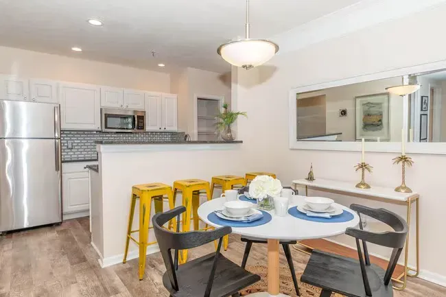 Dining area with a round table, black chairs, and yellow bar stools. Kitchen in background at Quarry in Columbus, OH.