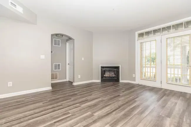 Empty living room with fireplace, arched doorway, and French doors to a balcony. Gray walls and wood-look floors at Quarry in Columbus, OH.