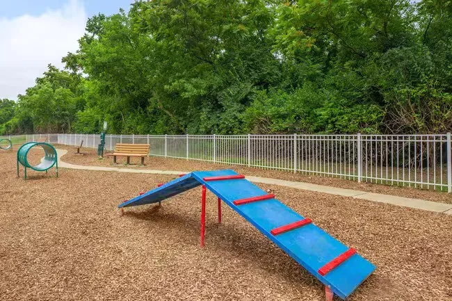 Dog park with blue agility equipment and white fence, surrounded by trees and mulch at Quarry in Columbus, OH.