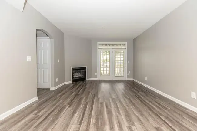 Empty living room with gray walls, wood-look flooring, fireplace, and double doors at Quarry in Columbus, OH.