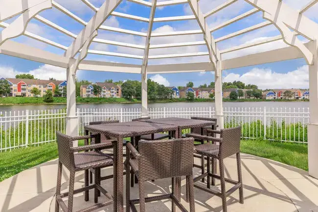 Gazebo with seating overlooking a lake, a white fence, and colorful apartments in the background at Quarry in Columbus, OH.