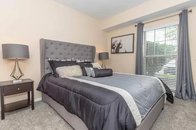 A bedroom with a gray bed, nightstands, and a window with gray curtains at Quarry in Columbus, OH.