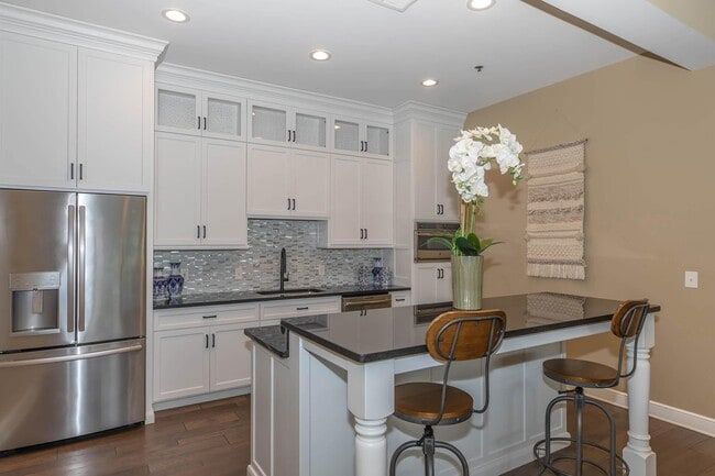 Bright white kitchen with a stainless steel fridge, black island, and beige wall. Two bar stools are at the island  at Quarry in Columbus, OH.