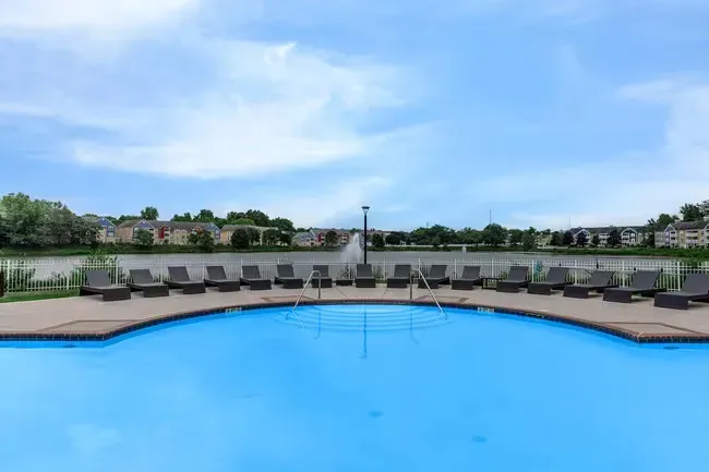 Blue pool with lounge chairs, overlooking a lake and buildings under a cloudy sky at Quarry in Columbus, OH.