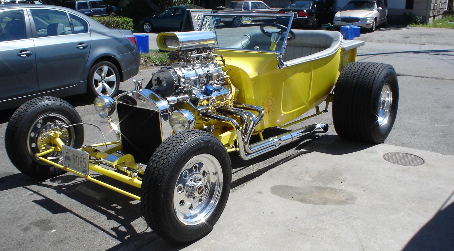 A yellow car with a chrome engine is parked in a parking lot