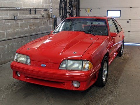 A red ford mustang with a hood scoop is parked in a garage.