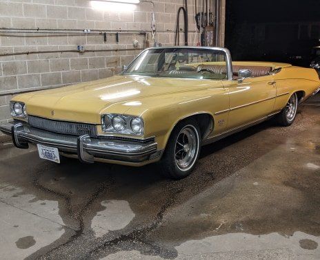 A yellow convertible car is parked in front of a brick wall.