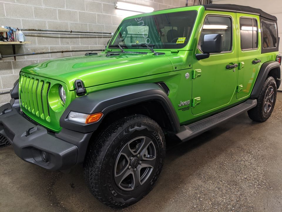 A green jeep wrangler is parked in a garage.