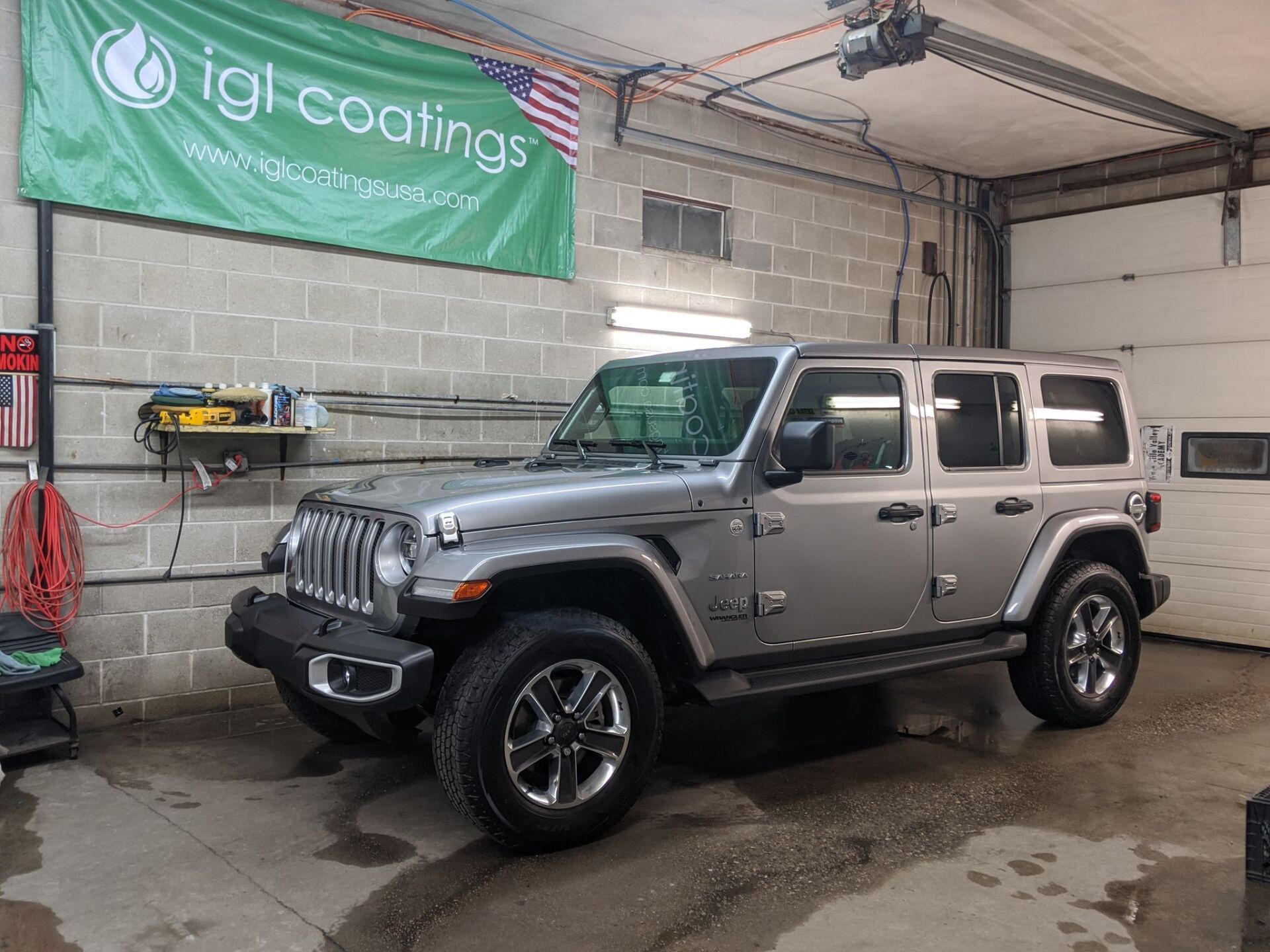 A silver jeep wrangler is parked in a garage under a green banner.