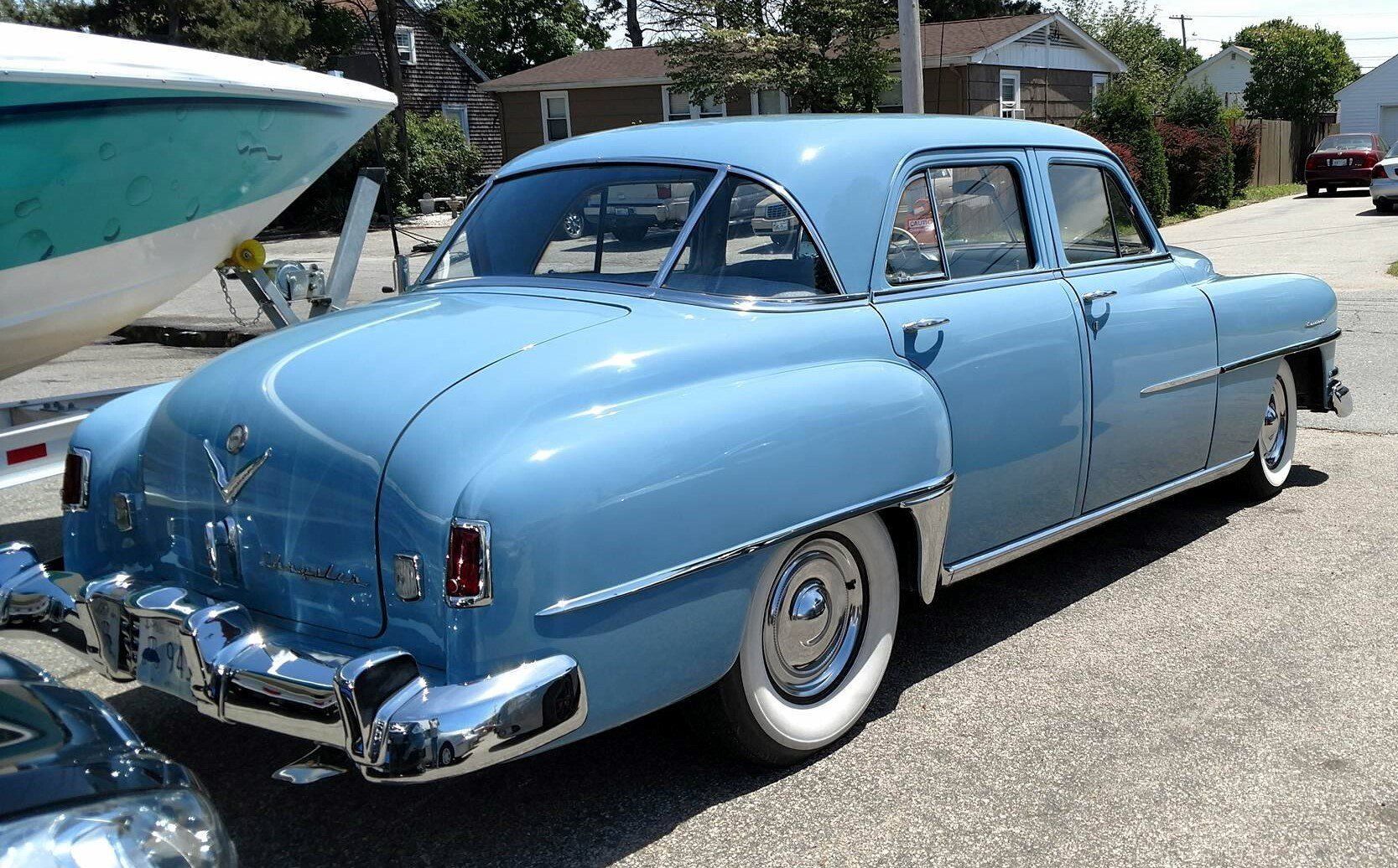 A blue car with white tires is parked next to a boat