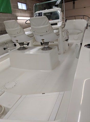 A white boat with two white chairs on the deck is sitting in a garage.