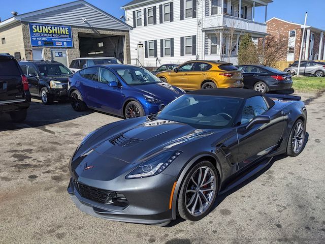 A gray sports car is parked in front of a sunshine car dealership.