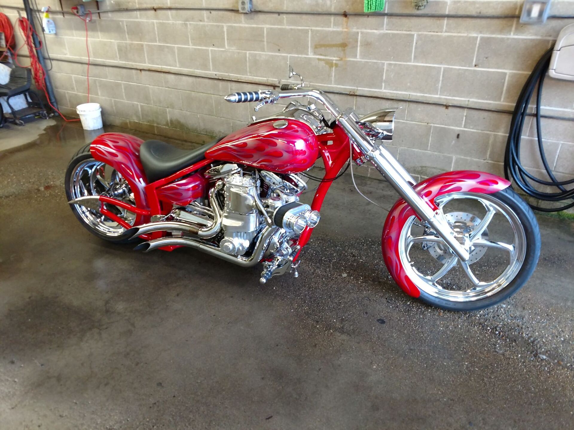A red motorcycle is parked in a garage next to a brick wall.