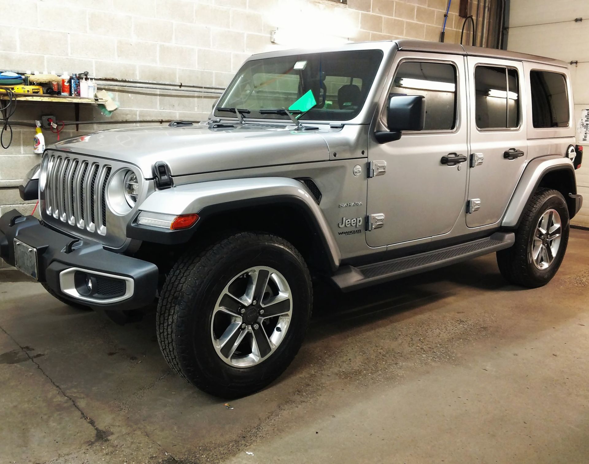 A silver jeep wrangler is parked in a garage.