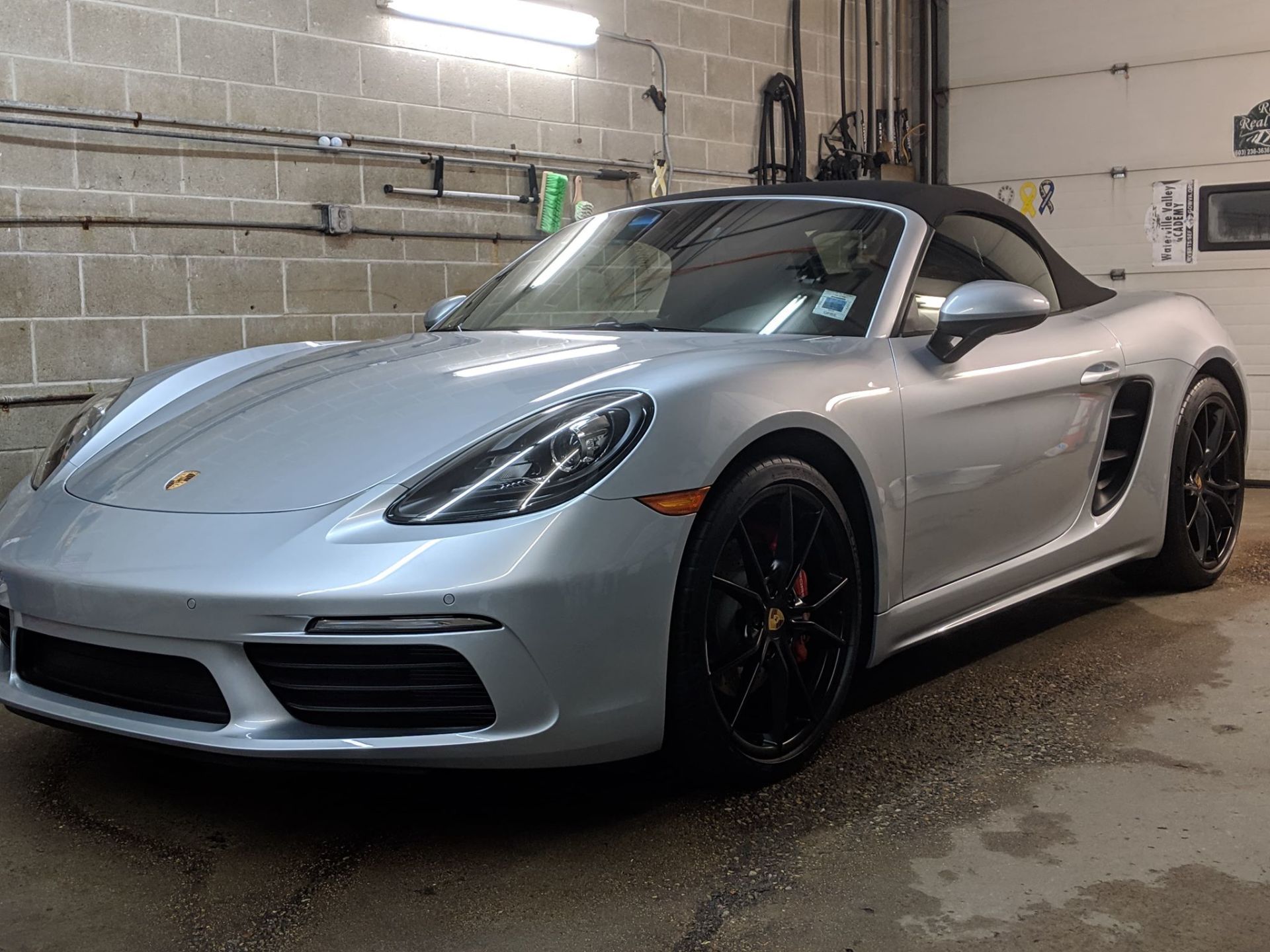 A silver porsche boxster convertible is parked in a garage.