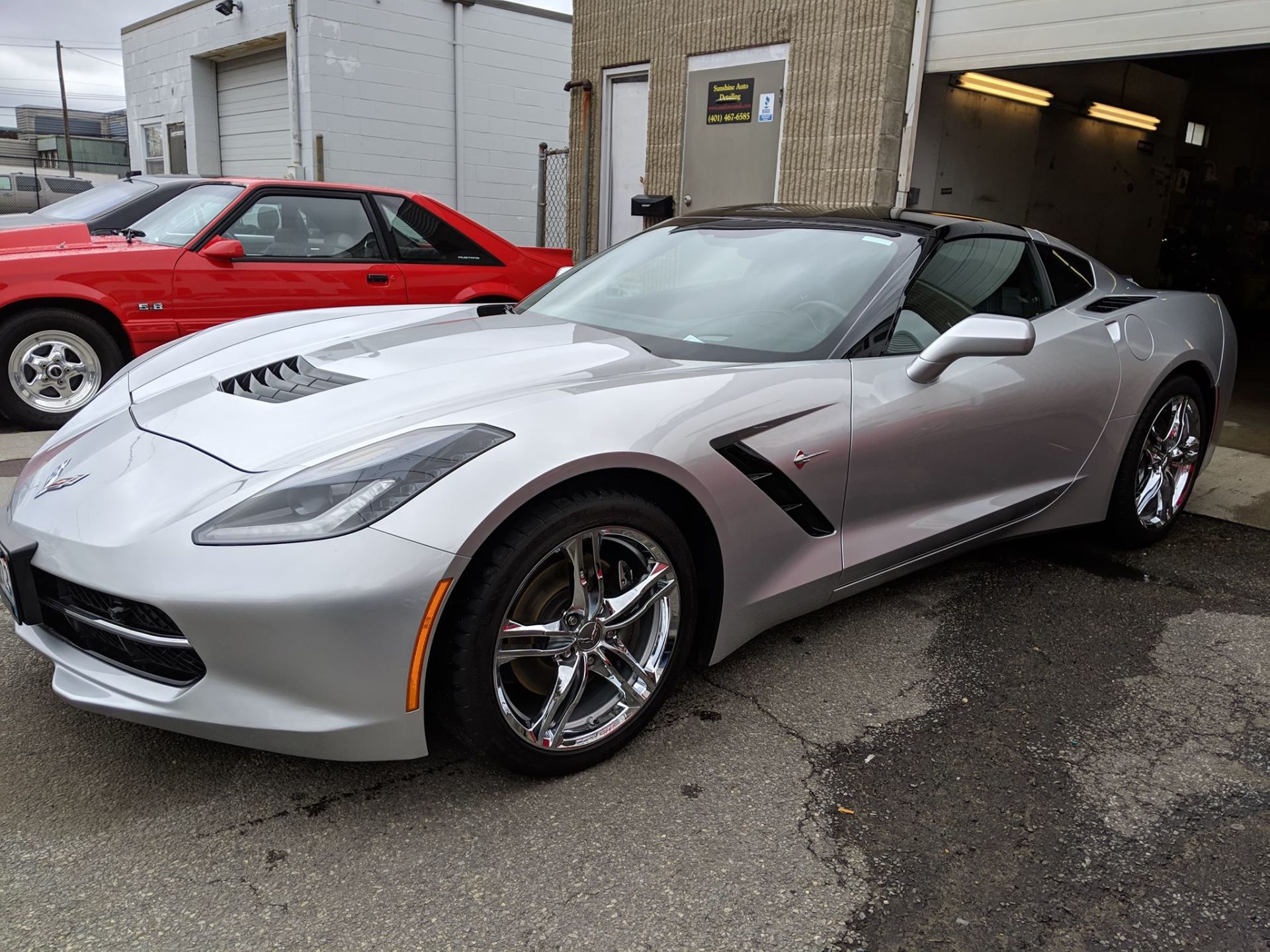 A silver corvette is parked next to a red mustang.