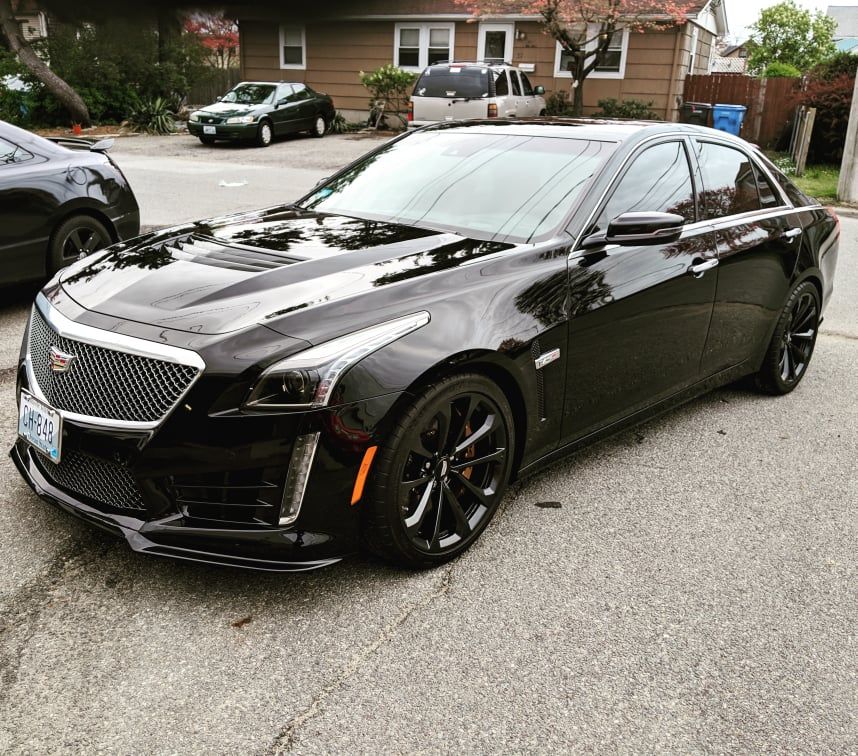 A black cadillac is parked in front of a house.