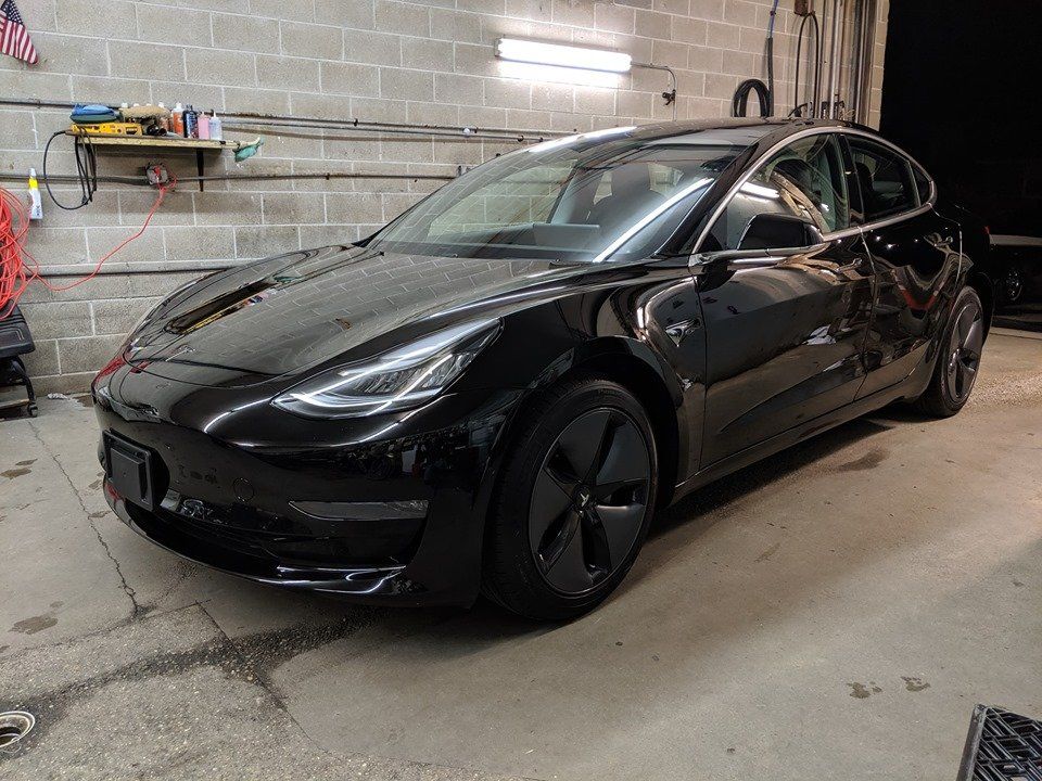 A black tesla model 3 is parked in a garage.