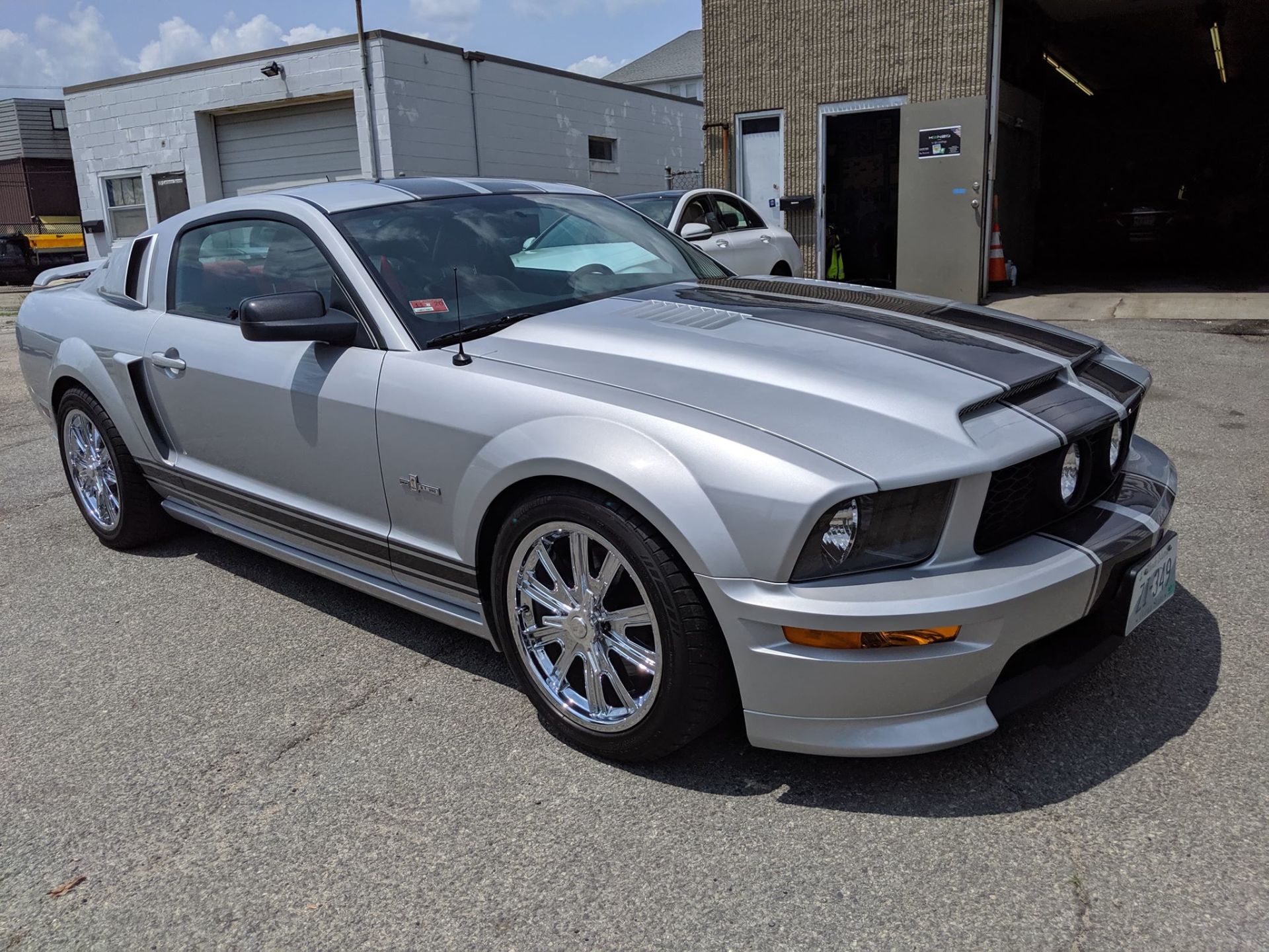 A silver mustang is parked in front of a garage.