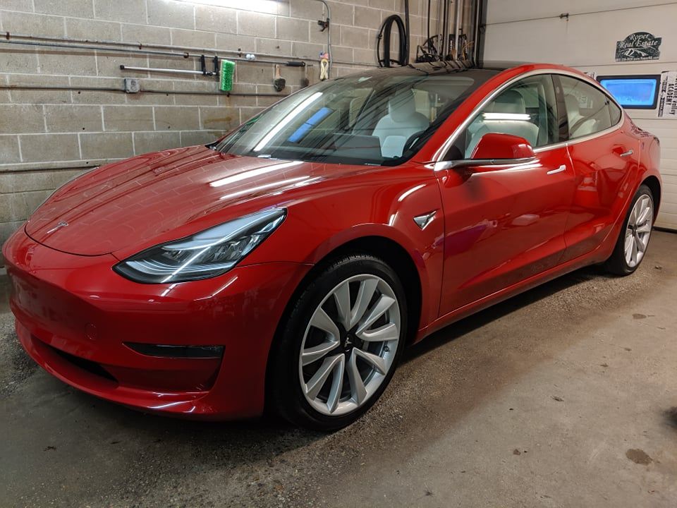 A red tesla model 3 is parked in a garage.