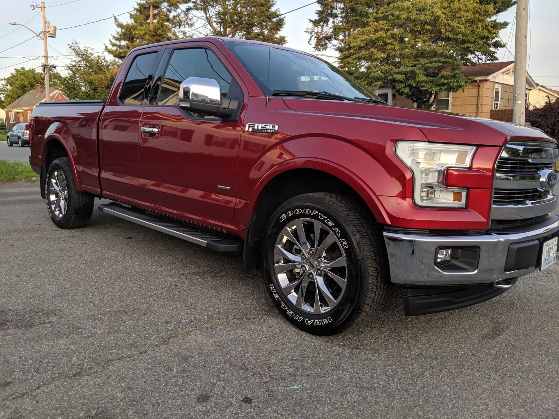 A red ford f150 truck is parked on the side of the road.