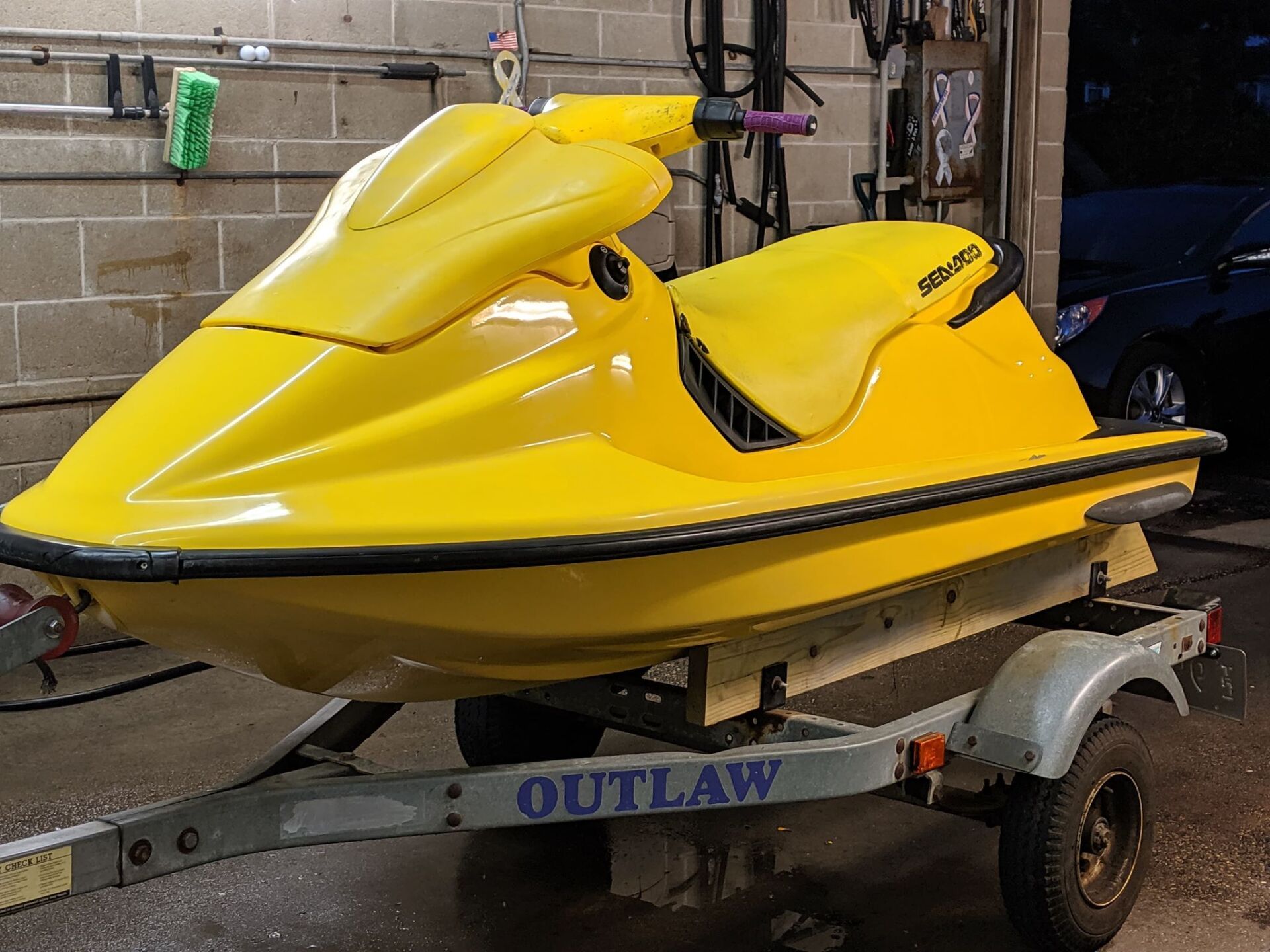 A yellow jet ski is on a trailer in a garage.