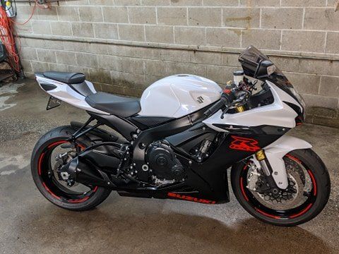 A white and black motorcycle is parked in front of a brick wall.