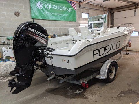 A white boat with a mercury outboard motor is parked in a garage.