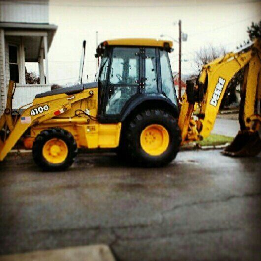 A yellow john deere backhoe is parked in front of a house