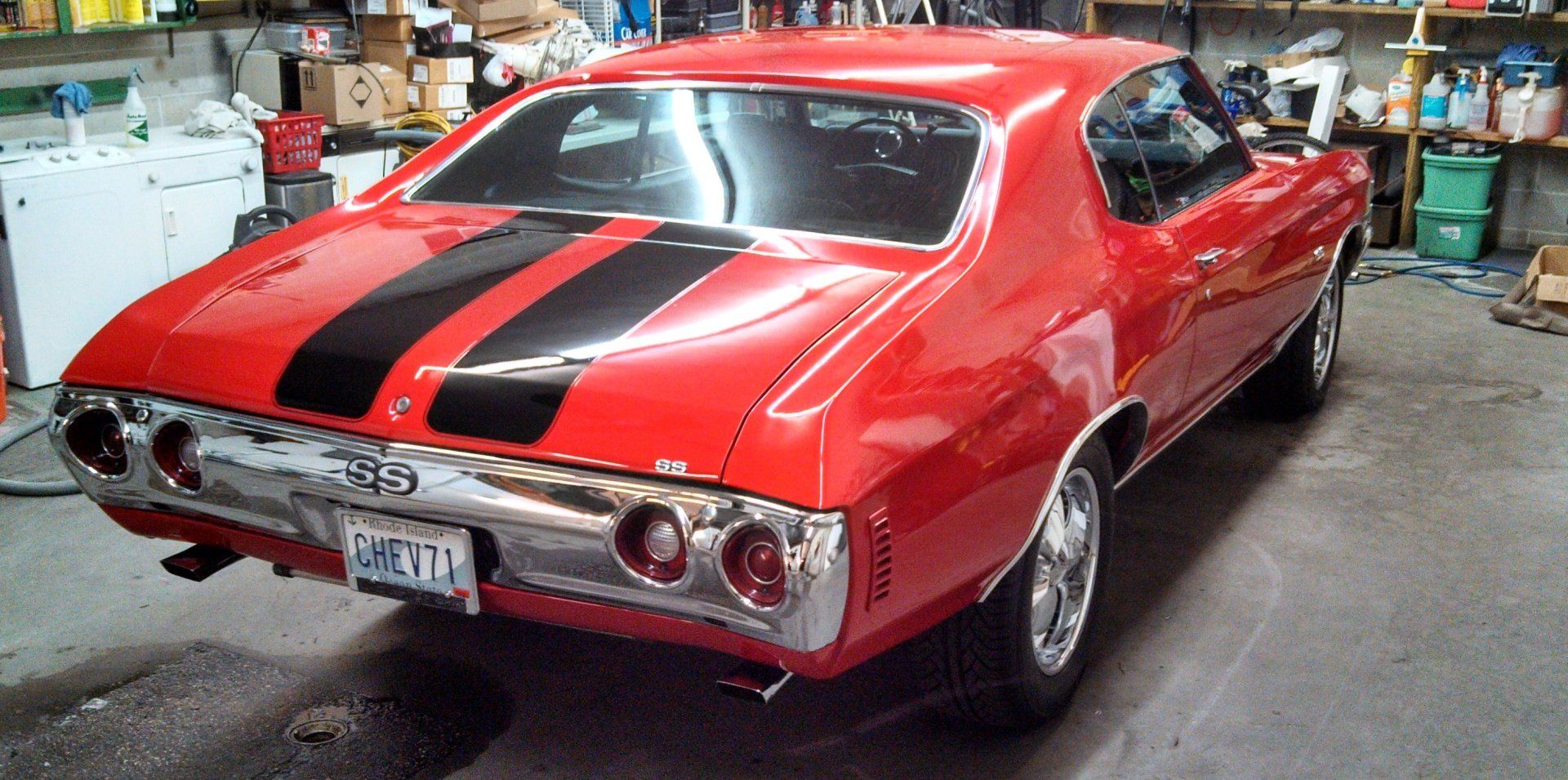A red car with black stripes is parked in a garage