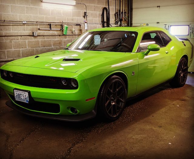 A bright green dodge challenger is parked in a garage