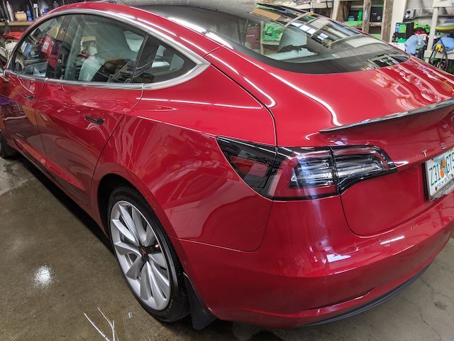 A red tesla model 3 is parked in a garage.