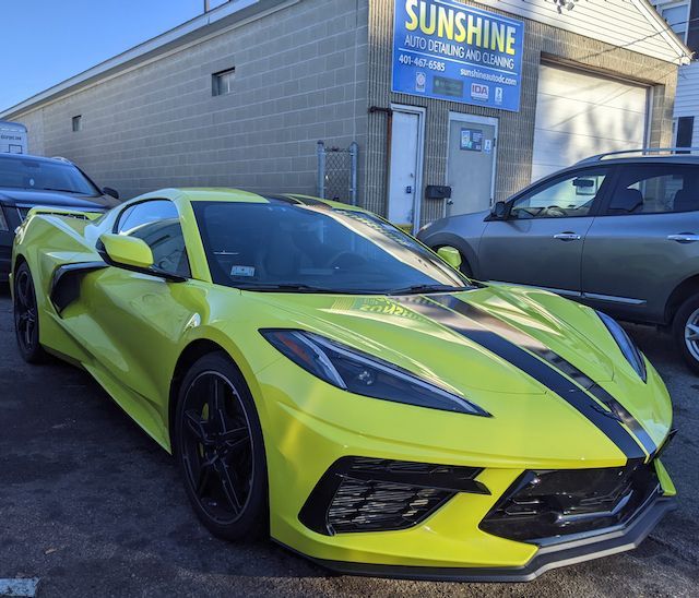 A yellow sports car is parked in front of a sunshine auto dealership