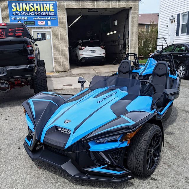 A blue and black slingshot is parked in front of sunshine auto detailing and cleaning