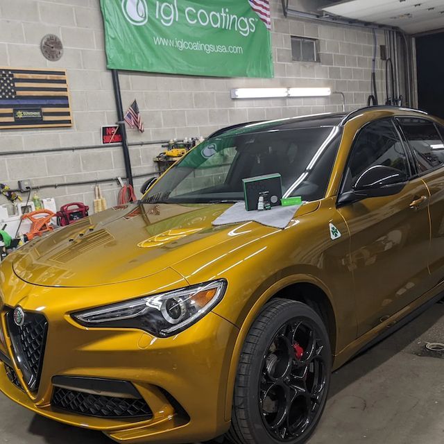 A yellow car is parked in front of a sign that says tgi coatings