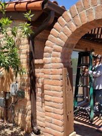 A man is standing on a ladder next to a brick archway.