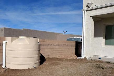 A water tank is sitting in the dirt in front of a house.