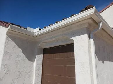 A white house with a brown garage door and a white gutter.
