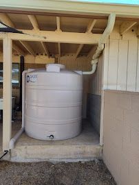 A large white water tank is sitting under a roof next to a house.