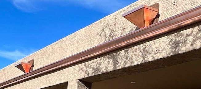 A close up of a gutter on the side of a building with a blue sky in the background.