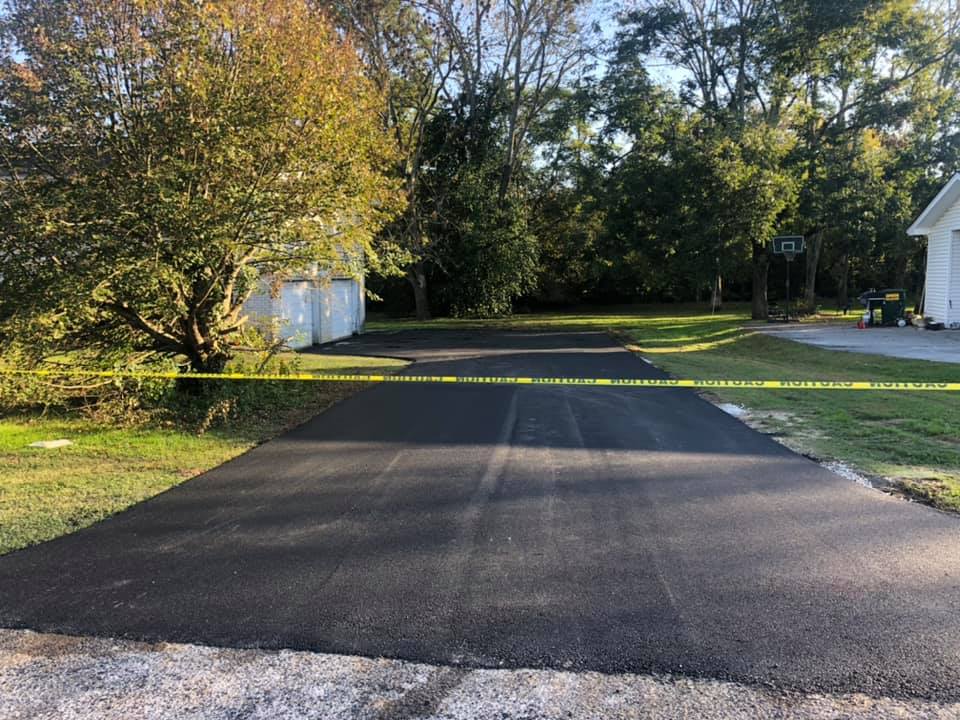 A newly paved driveway is surrounded by trees and grass.