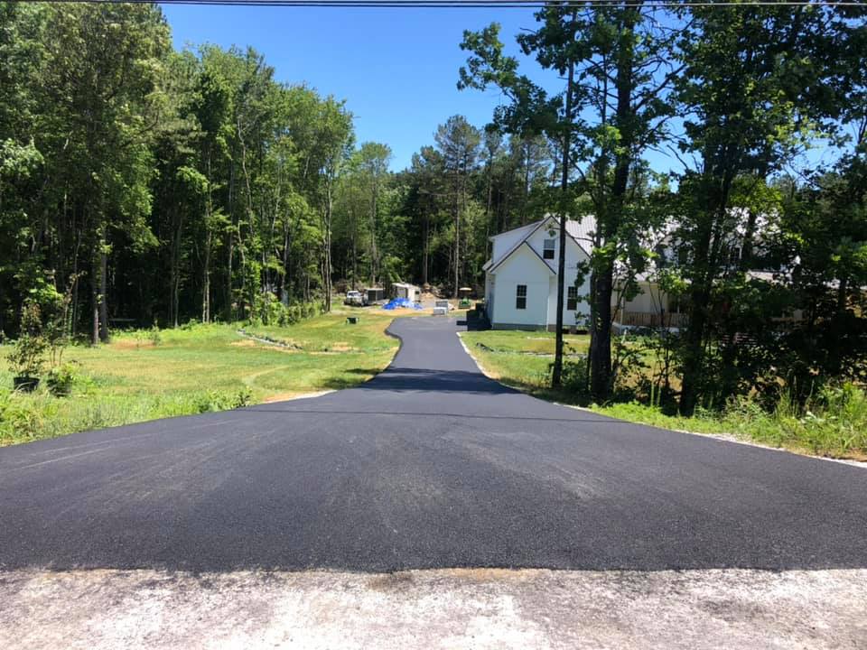 A road with a house in the background and trees on both sides