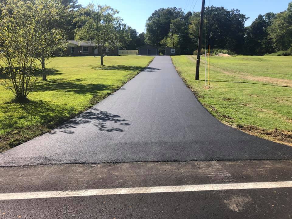 A newly paved driveway going through a grassy field.