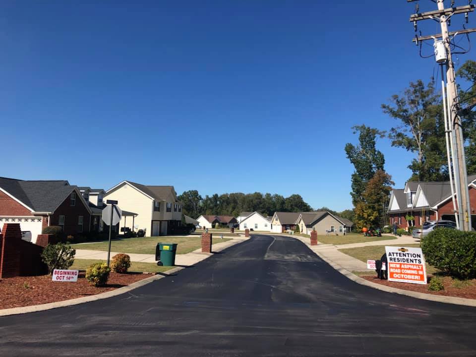 A newly paved road in a residential neighborhood with houses on both sides.