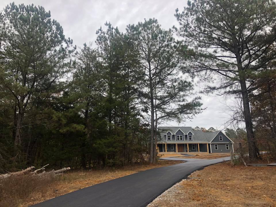 A large house with a large porch is sitting on top of a dirt field.