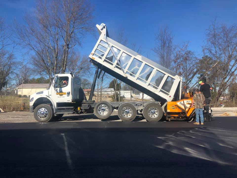 A dump truck is being loaded with asphalt on a road.