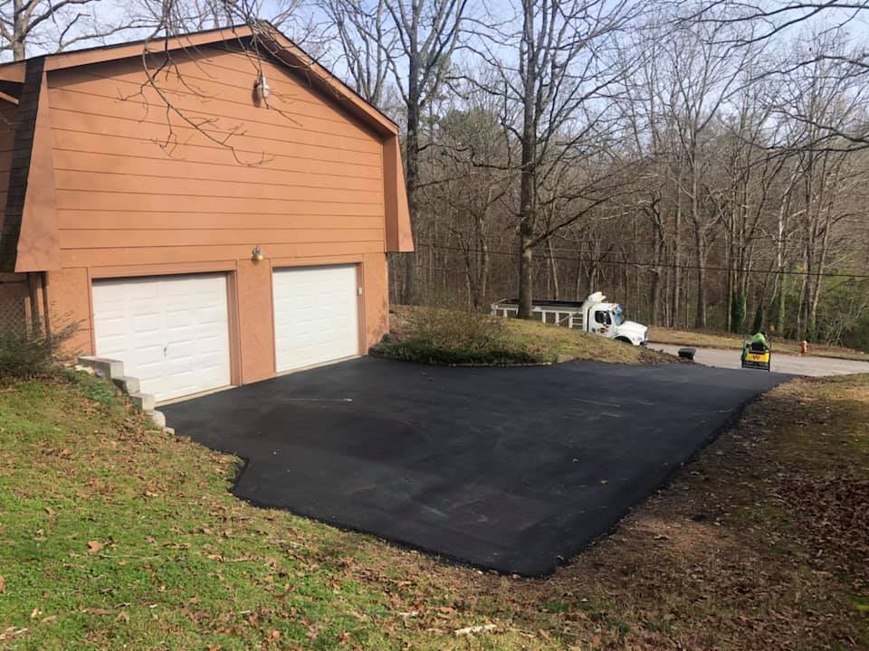 A garage with two garage doors and a black driveway in front of it.