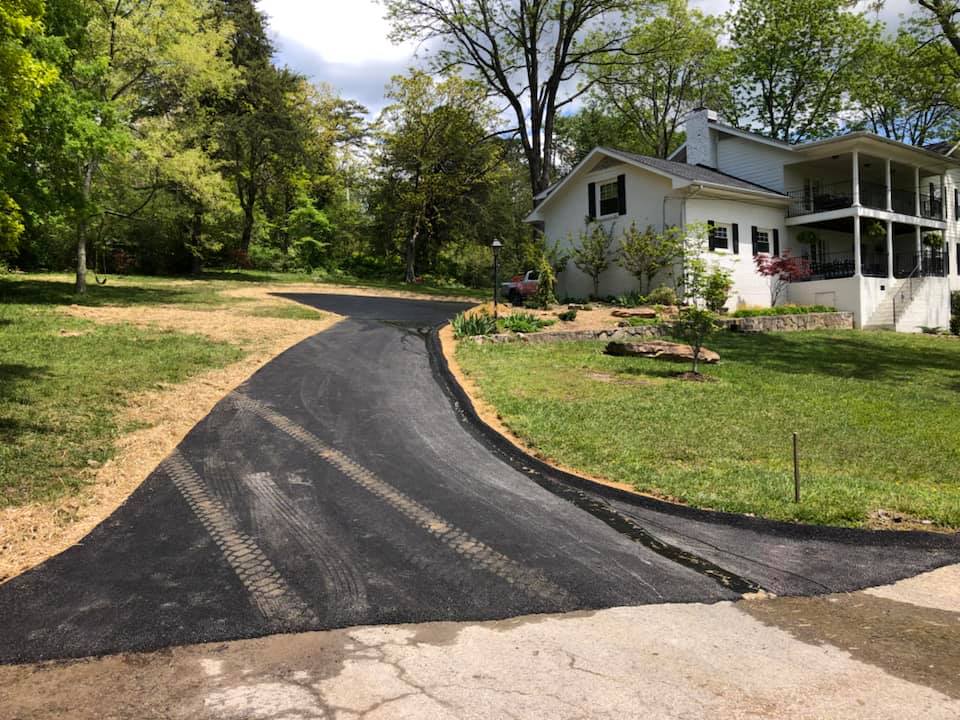 A driveway leading to a large white house surrounded by trees and grass.