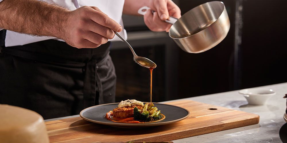 Un chef verse de la sauce sur un morceau de viande dans une assiette.