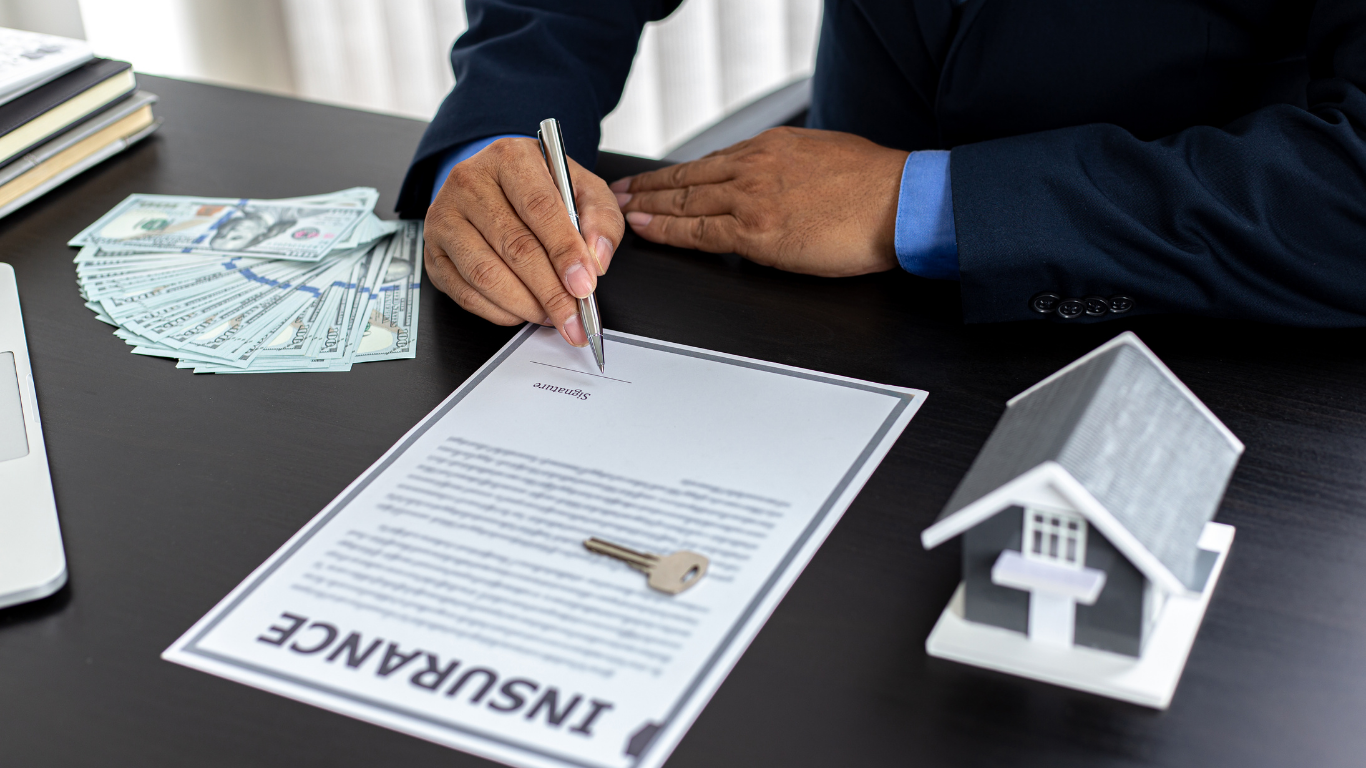 A man is signing a document next to a model house and money.